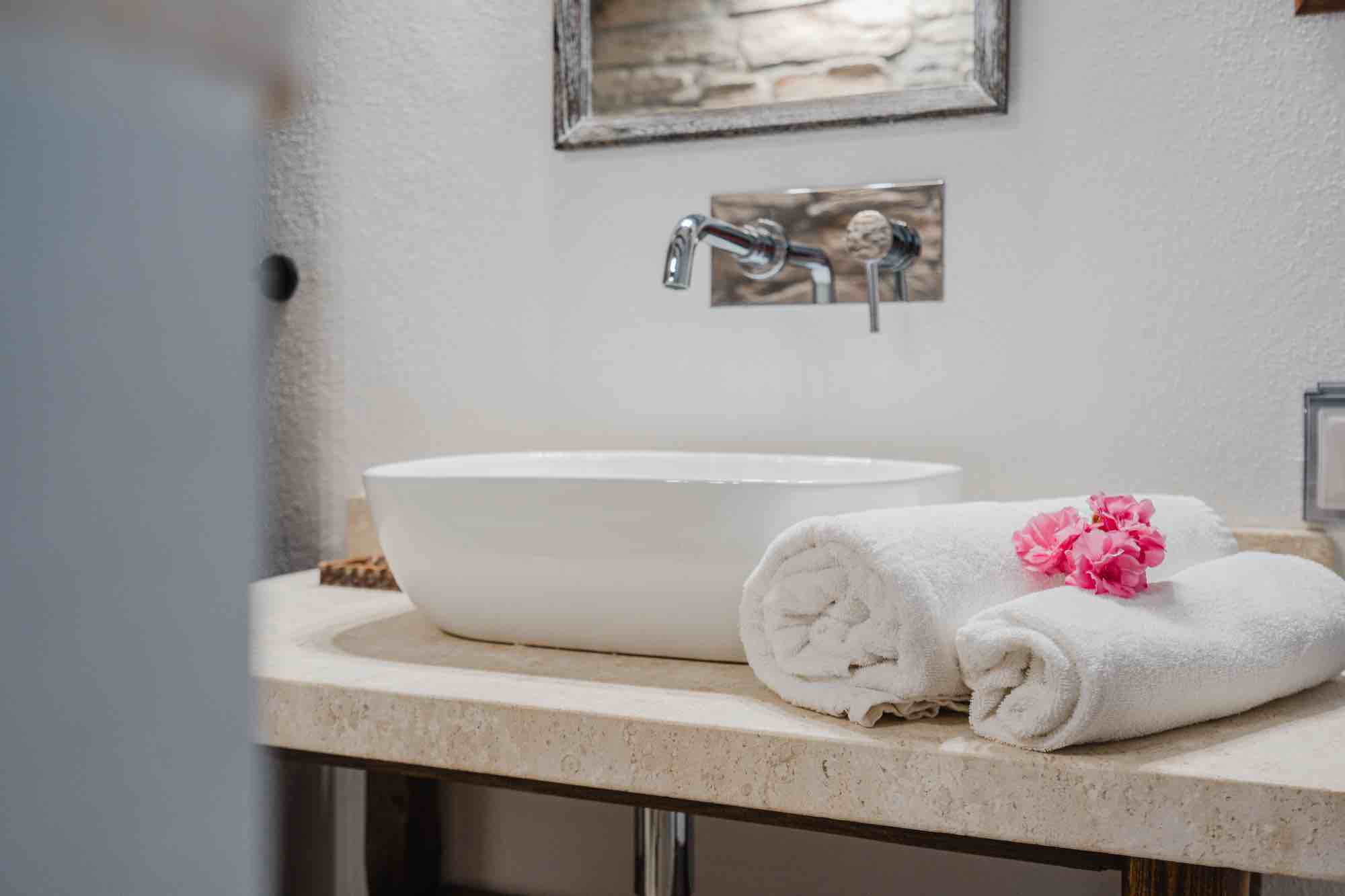 Dettaglio del bagno di una villa di lusso in Sardegna con asciugamani piegati e fiori, che trasmette pulizia e cura