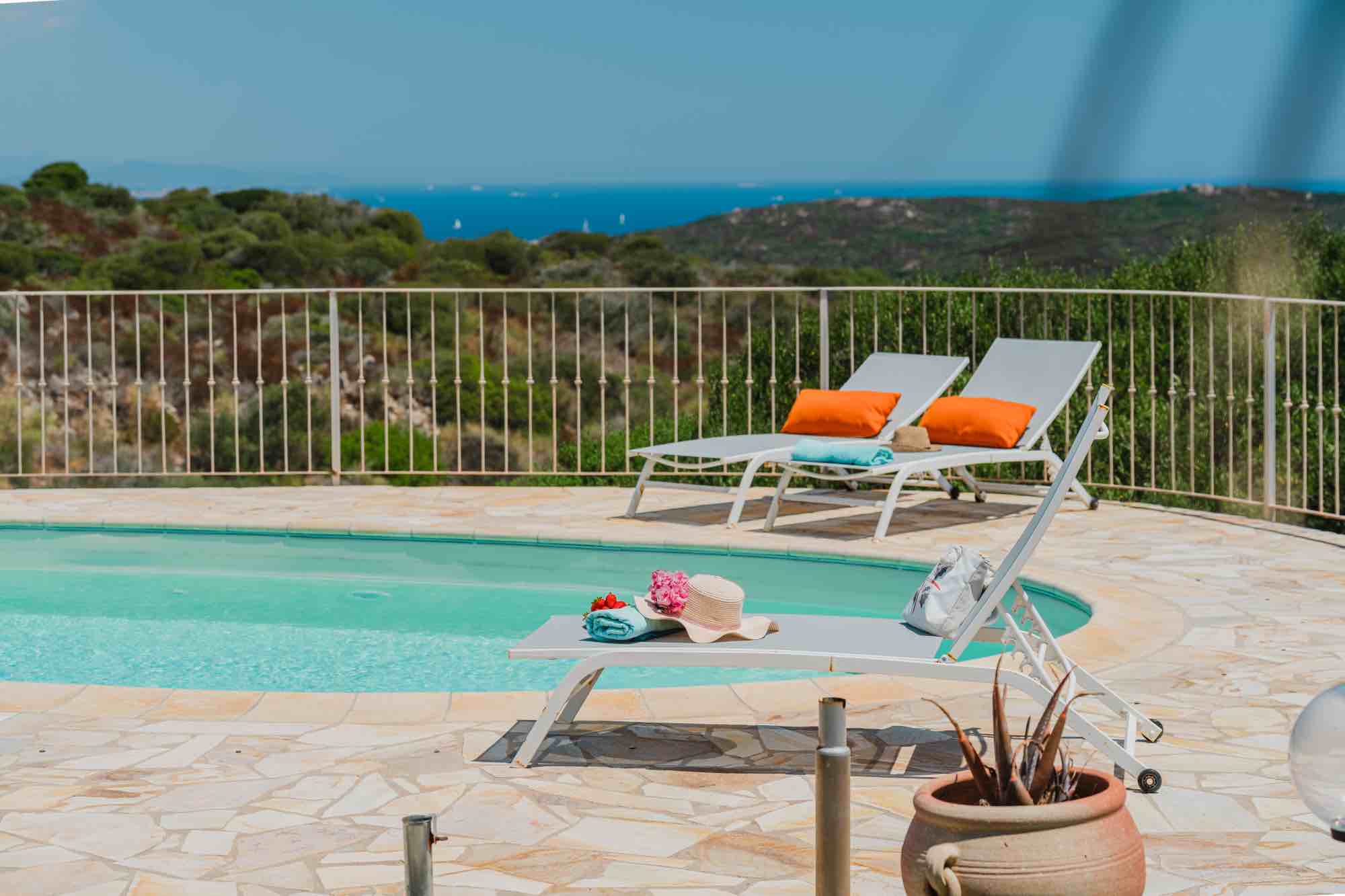 Dettaglio a bordo piscina in Sardegna con lettini, asciugamani, cappello e vista sul mare
